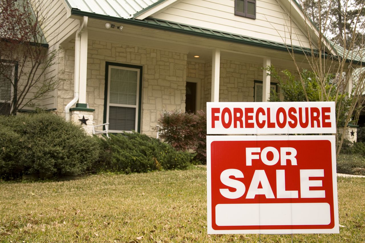 A for sale sign indicating a foreclosure is posted in front of a house